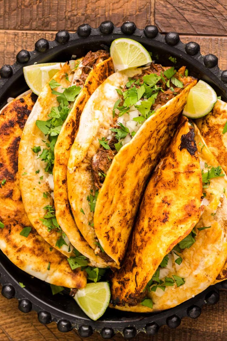 Birria tacos on a black plate on a wooden table.