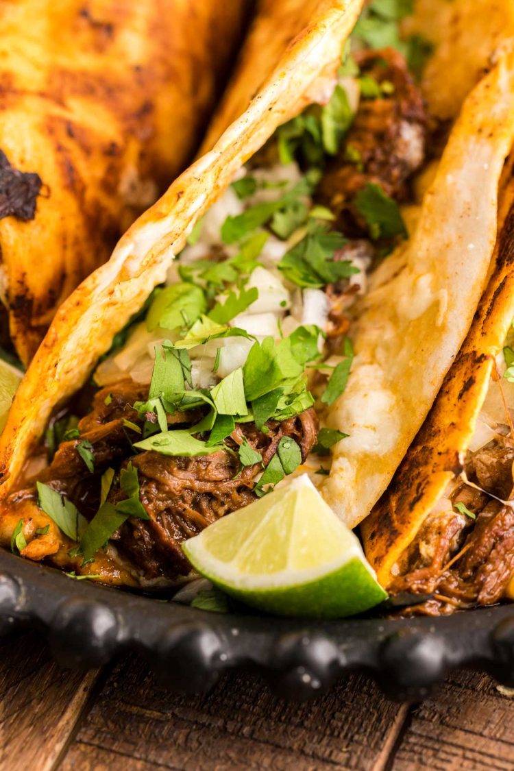 Close up of a birria taco on a black plate with more tacos.