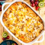 Overhead photo of a biscuits and gravy casserole on a wooden table with fruits and serving plates around it.