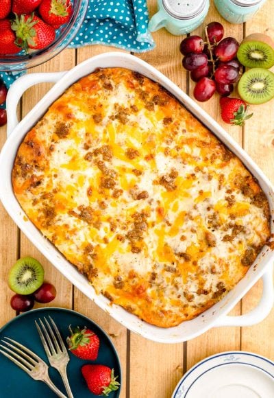 Overhead photo of a biscuits and gravy casserole on a wooden table with fruits and serving plates around it.