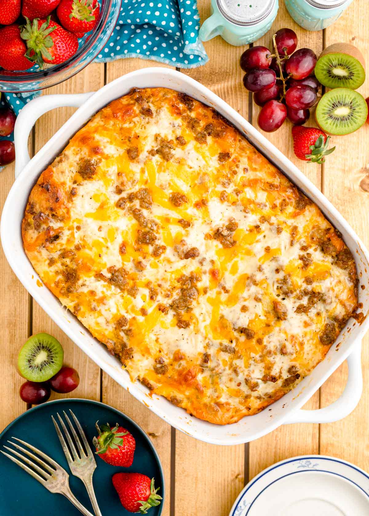 Overhead photo of a biscuits and gravy casserole on a wooden table with fruits and serving plates around it.