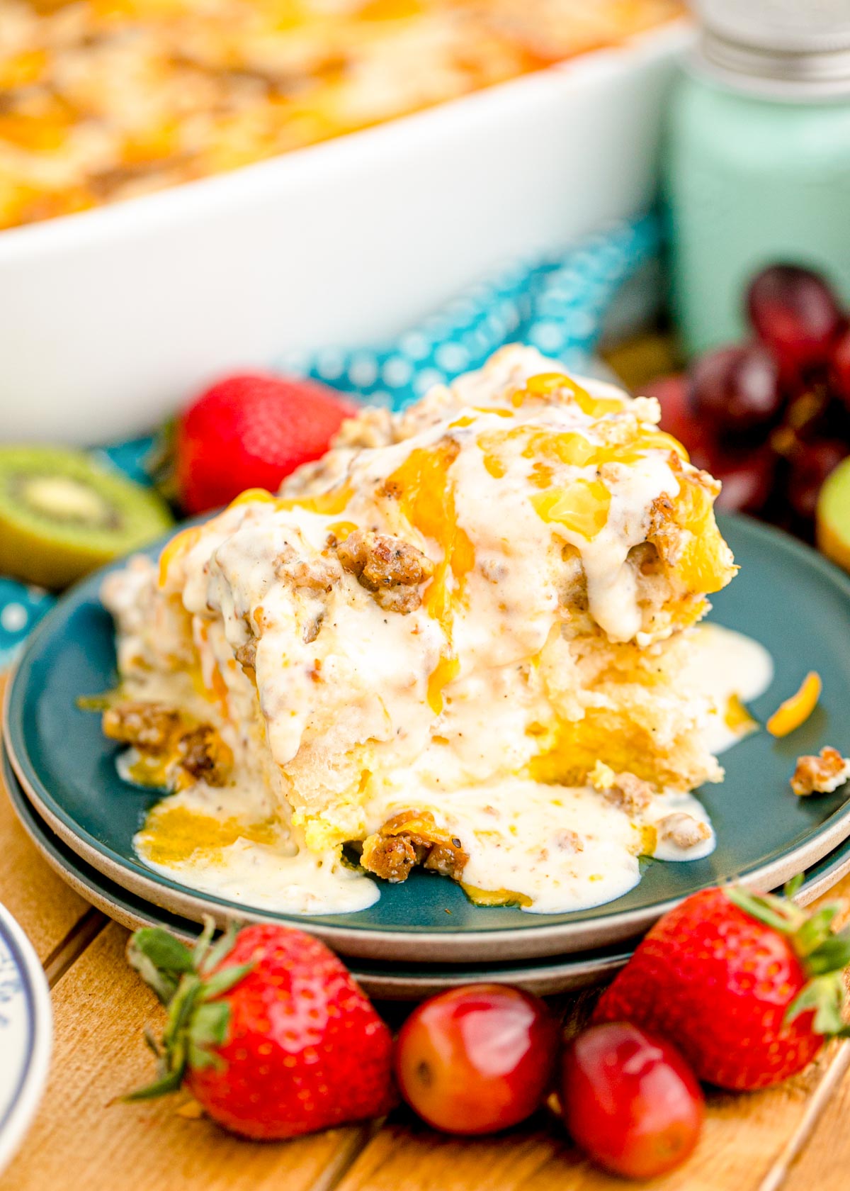 A slice of biscuits and gravy casserole on a blue plate surrounded by berries.