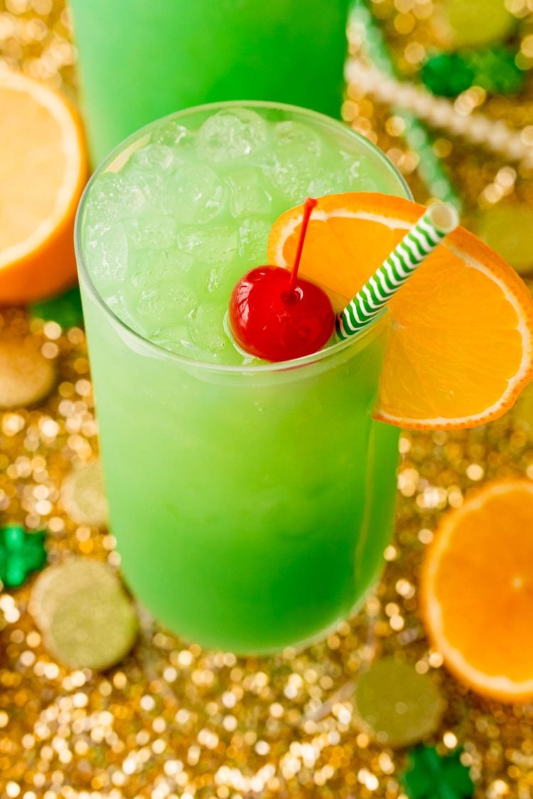 Highball glass filled with a green cocktail garnished with orange slice and maraschino cherry.