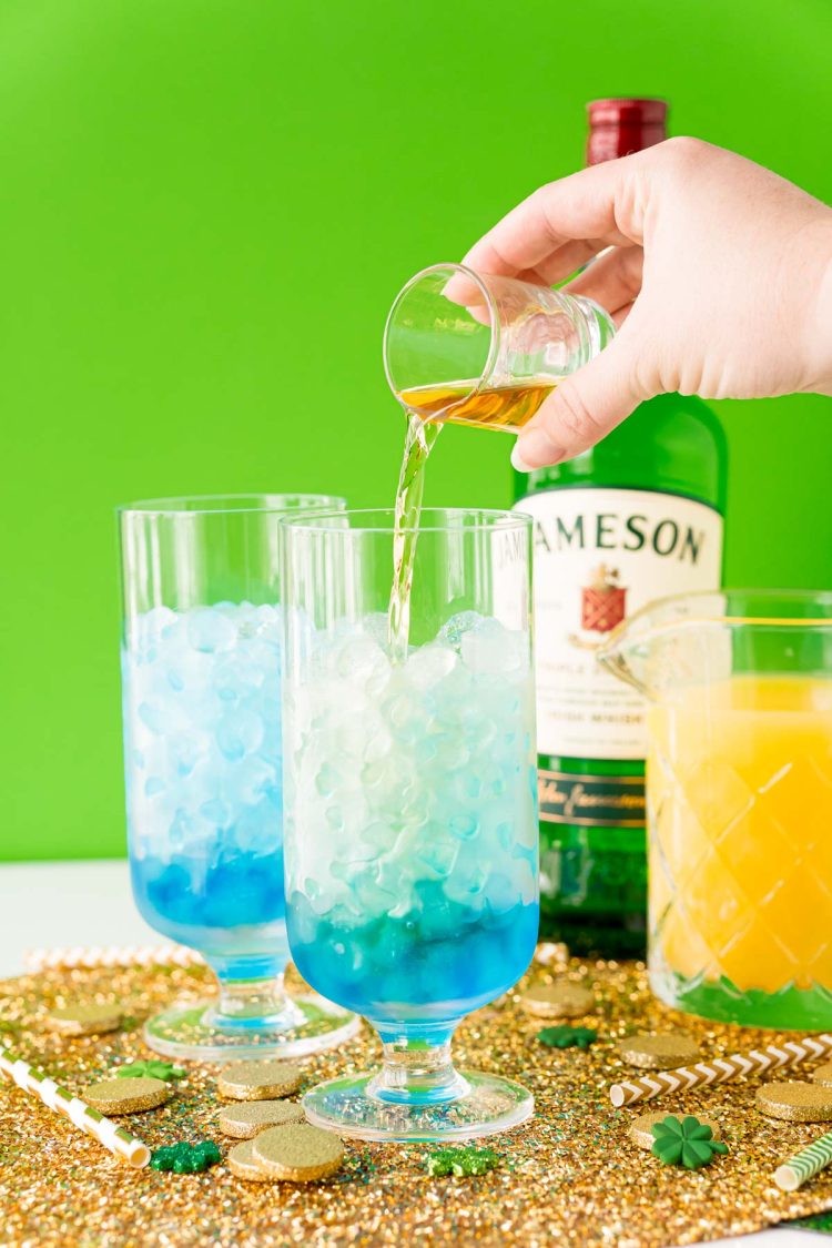 Irish whiskey being poured into a glass with ice and blue curacao.