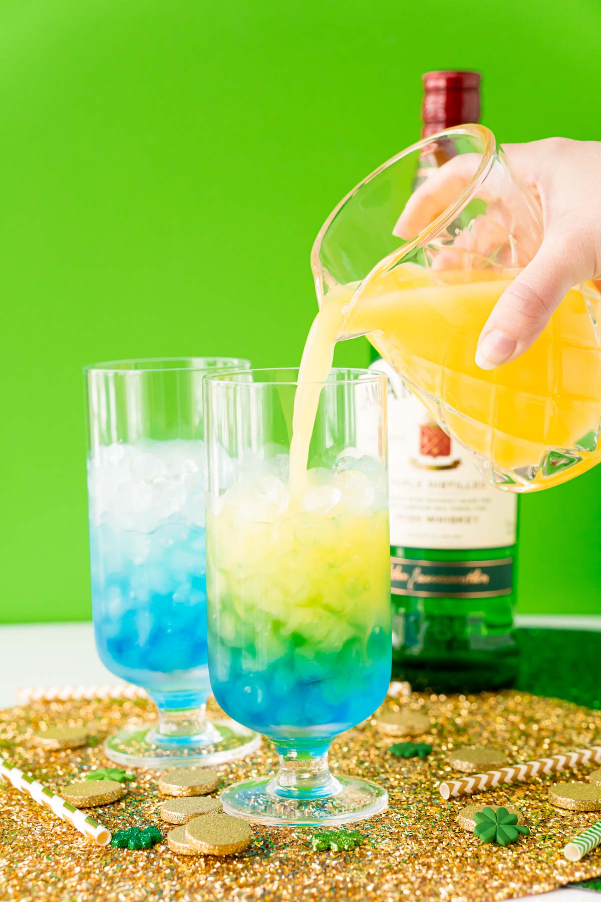 Orange juice being poured into a cocktail glass with whiskey and blue curacao.