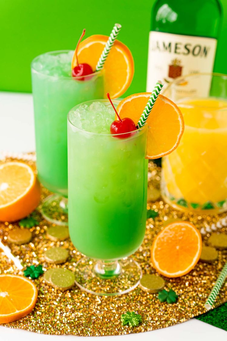 Two glasses filled with a green cocktail on a gold placemat.