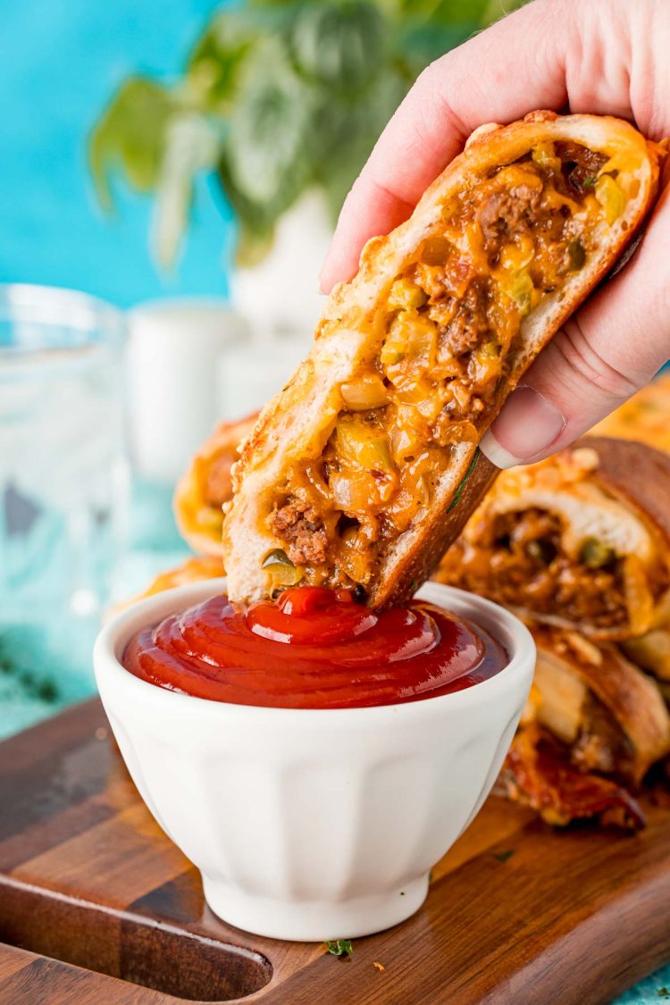 A woman's hand holding a piece of garbage bread and dipping it in a bowl of ketchup.