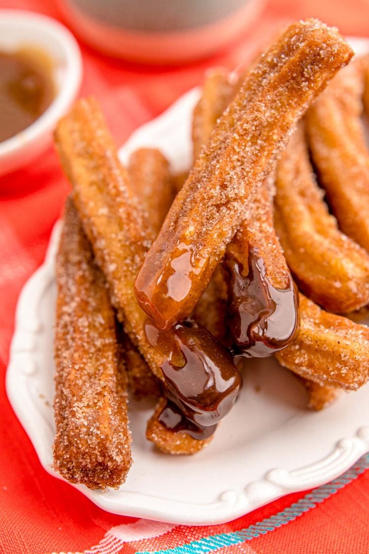 Churros on a white plate on an orange napkin.