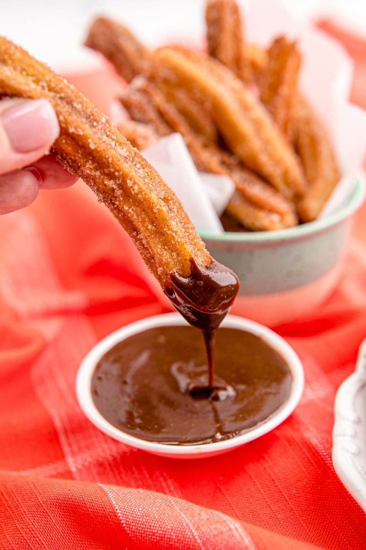Close up photo of a woman's hand dunking a churro in chocolate sauce.