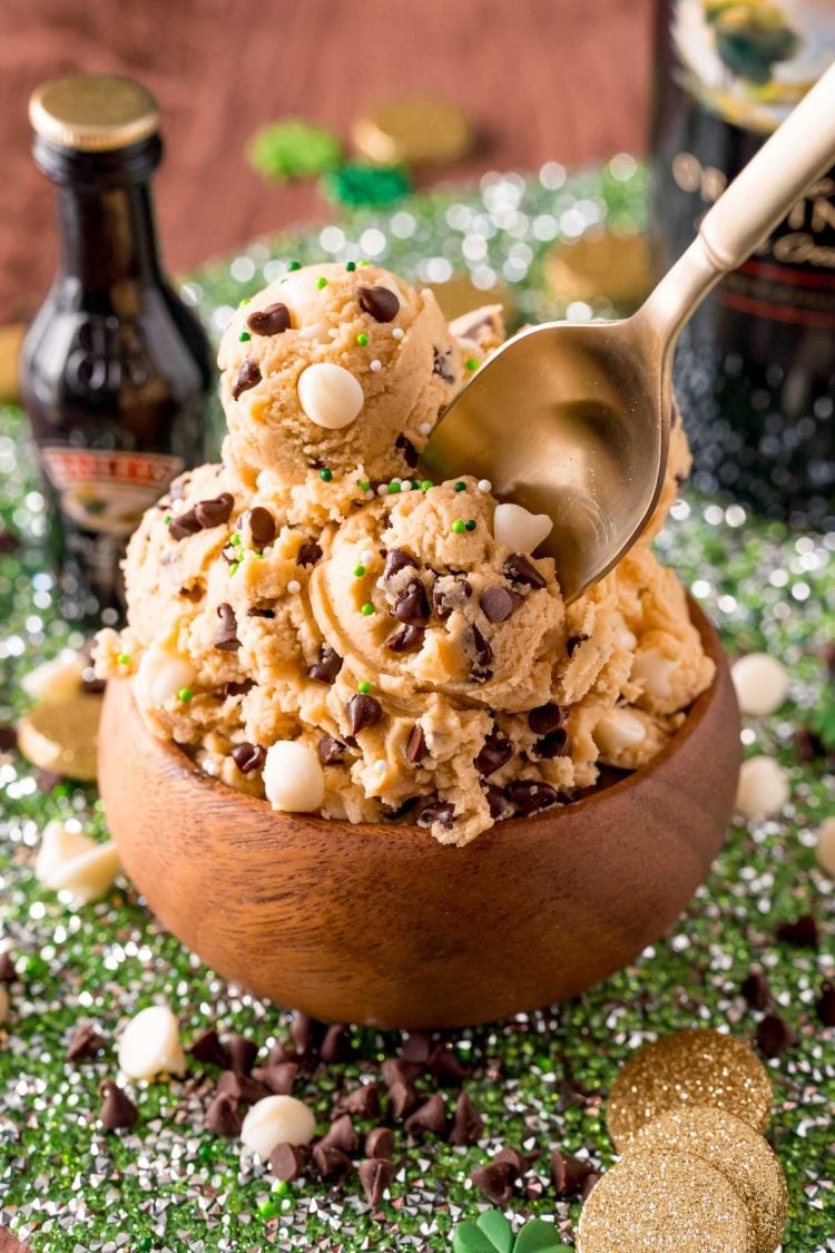 A spoon taking a bite of Irish cream cookie dough out of a wooden bowl.