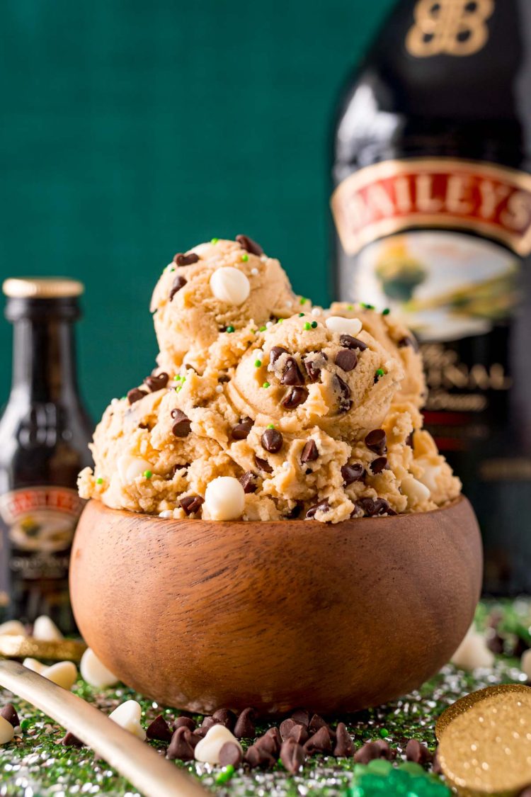 Edible cookie dough in a wooden bowl with a bottle of Irish cream in the background.