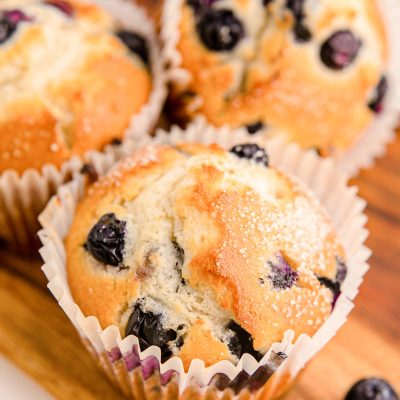 Three blueberry muffins on a wooden tray.