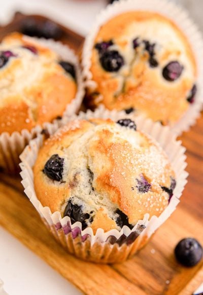 Three blueberry muffins on a wooden tray.