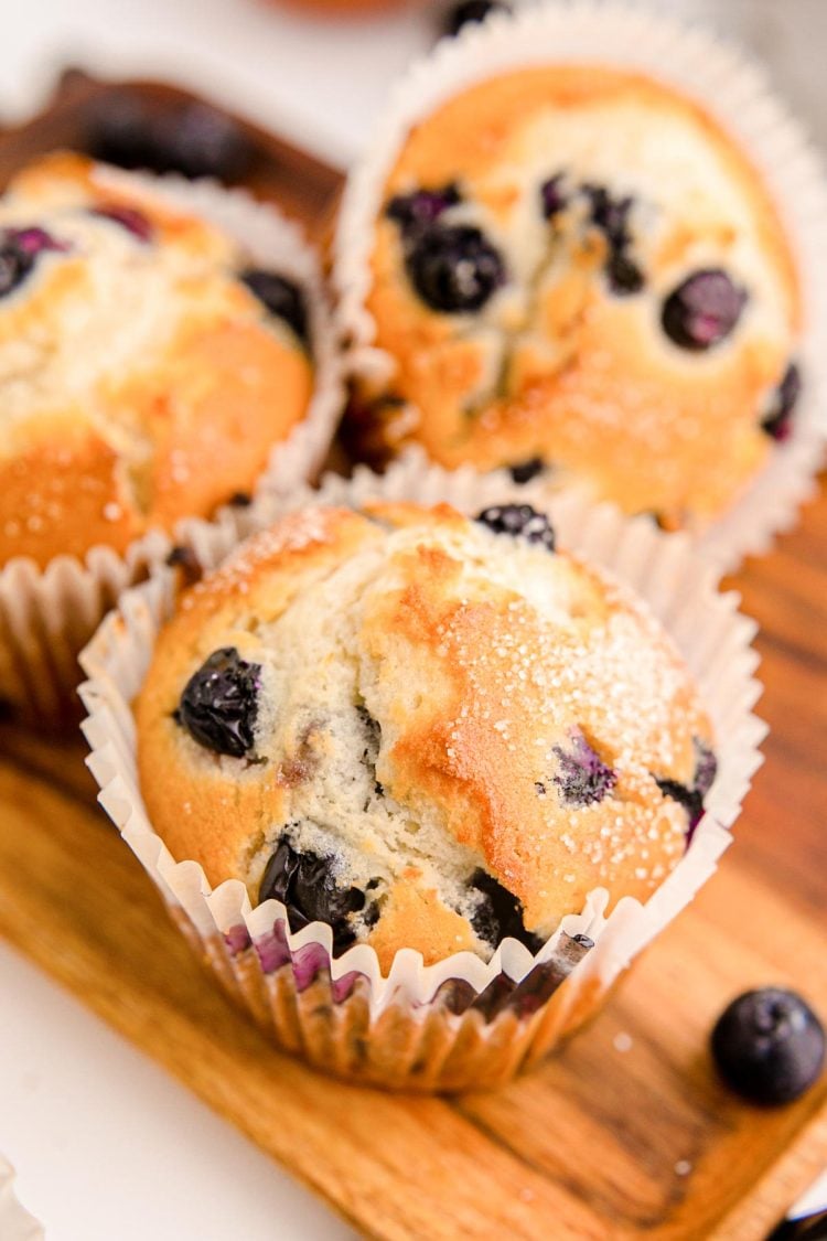 Three blueberry muffins on a wooden tray.