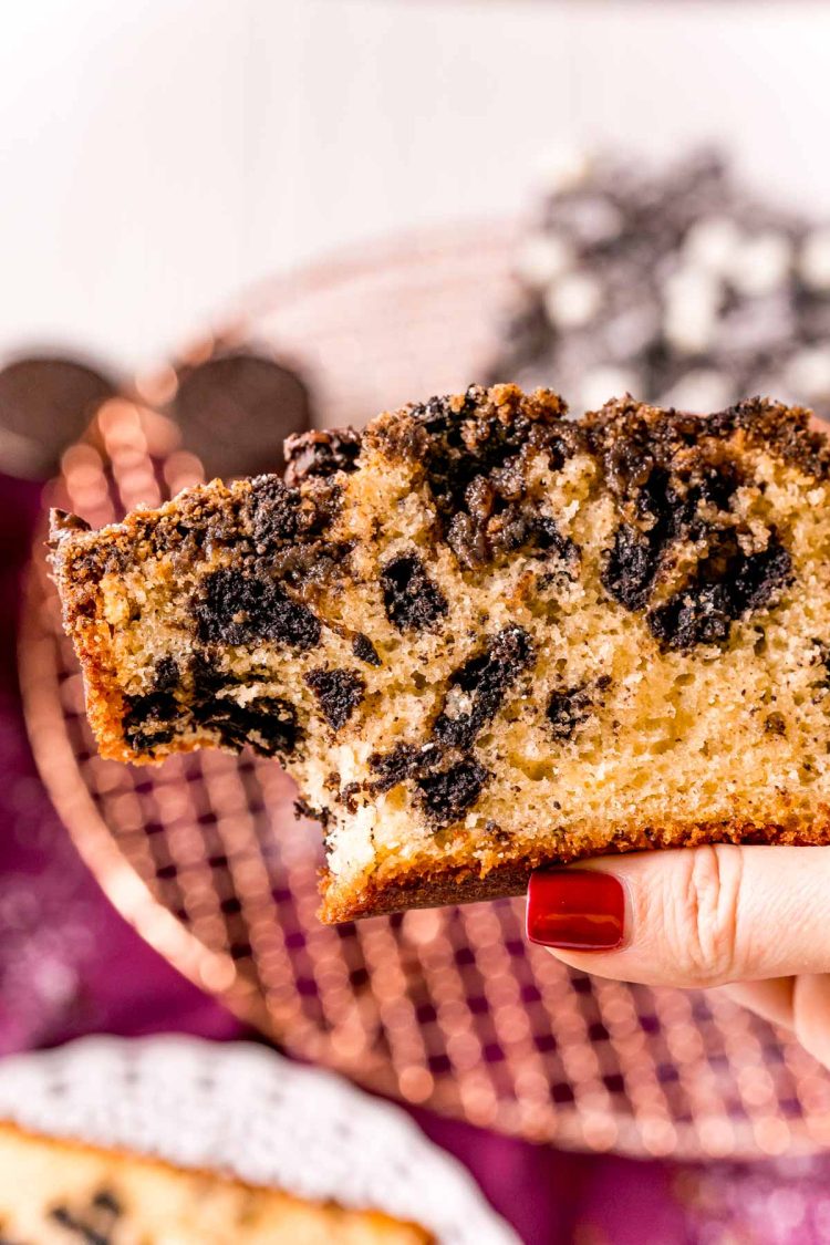 A woman's hand holding a slice of Oreo coffee cake with a bite taken out if it.