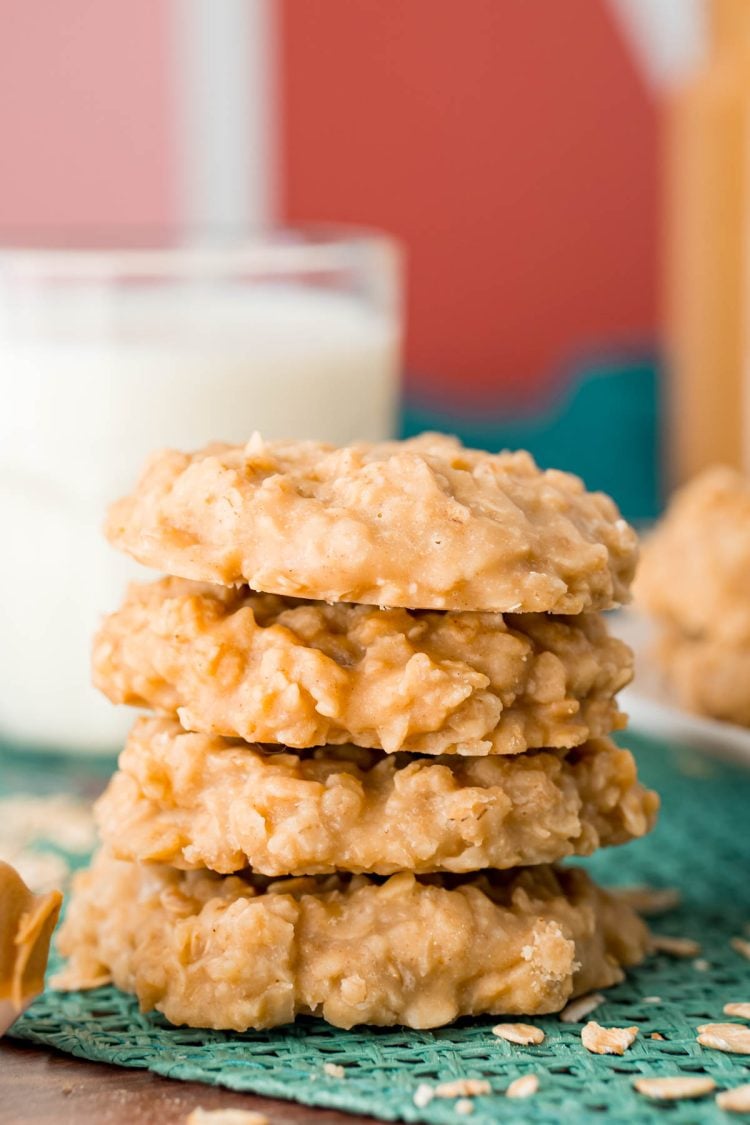 A stack of four peanut butter flavored no bake cookies on a teal placemat with a glass of milk in the background.