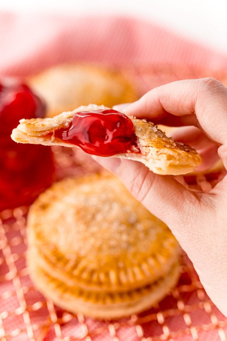 A woman's hand holding a cherry hand pie to the camera.