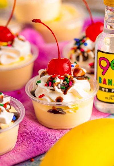 Close up photo of banana split pudding shots in plastic shot containers.