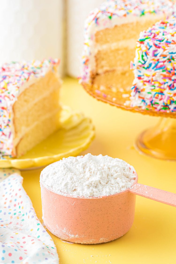 Cake flour substitute in a pink measuring cup on a yellow surface.
