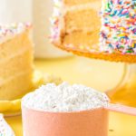 Cake flour substitute in a pink measuring cup on a yellow surface.