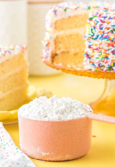 Cake flour substitute in a pink measuring cup on a yellow surface.