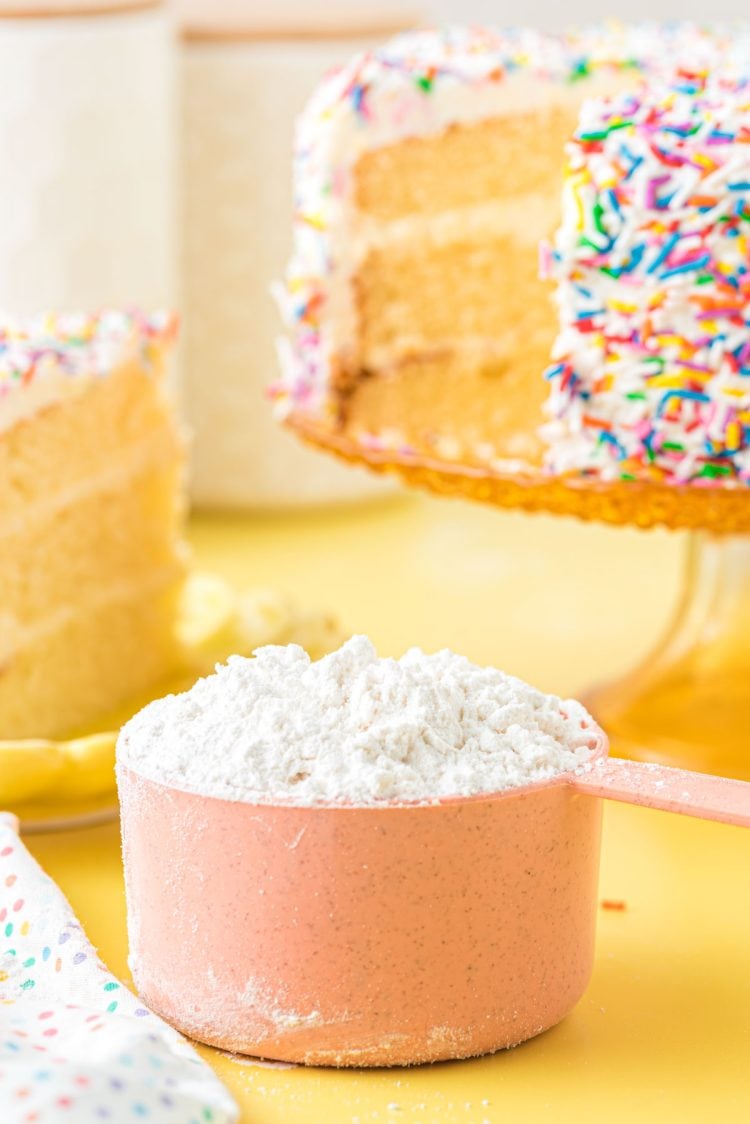 Cake flour substitute in a pink measuring cup on a yellow surface.