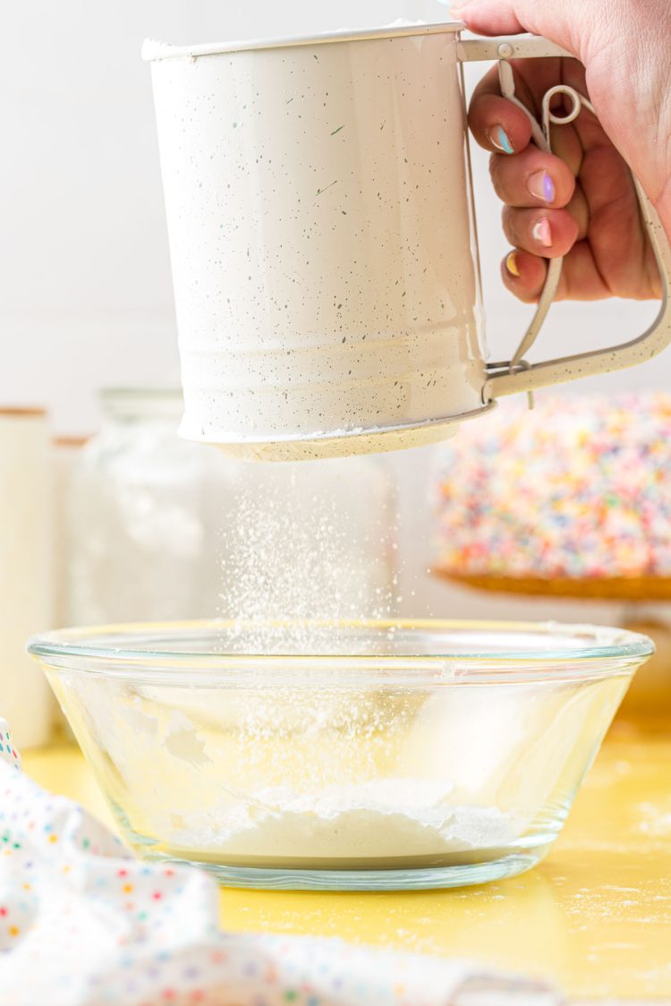 Cake flour substitute being sifted into a glass mixing bowl.