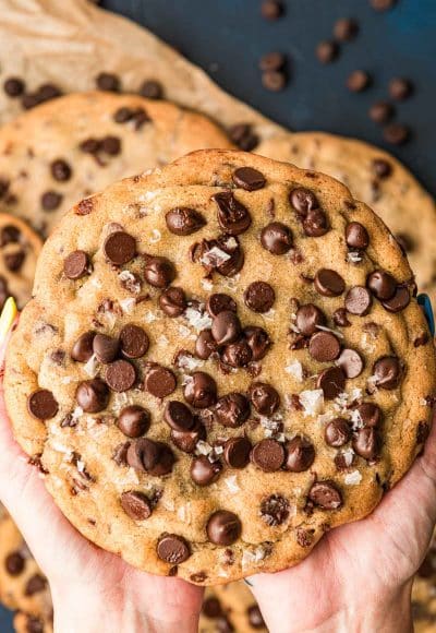 A woman's hands holding a giant chocolate chip cookies.