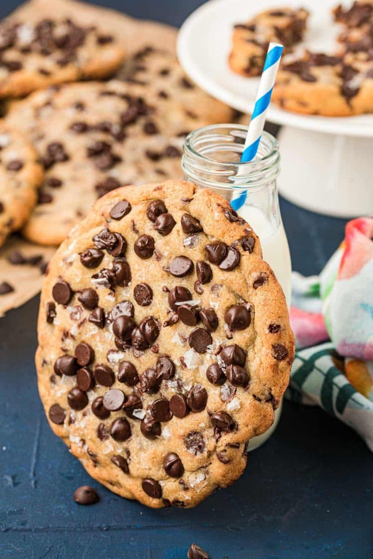 Giant chocolate chip cookie leaning against a bottle of milk.