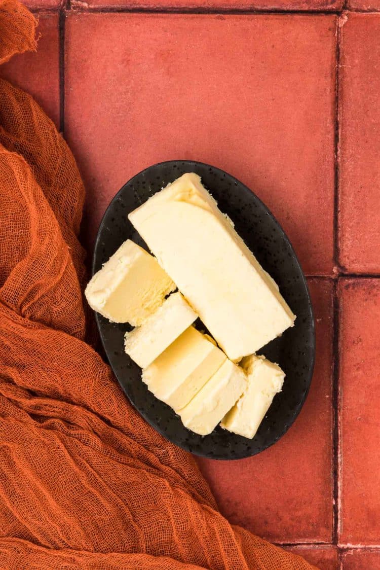 Butter in a black dish on a rust colored tile surface.