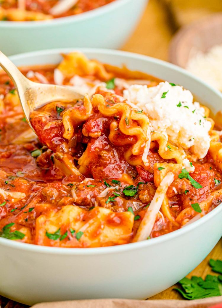 A spoon scooping abite of lasagna soup out of a bowl.