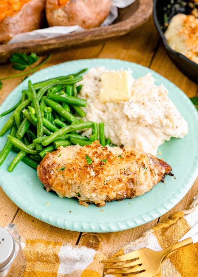 Parmesan crusted chicken on a blue plate with mashed potatoes and green beans.