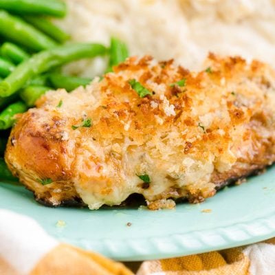 Close up photo of parmesan crusted chicken on a blue plate with mashed potatoes and green beans.