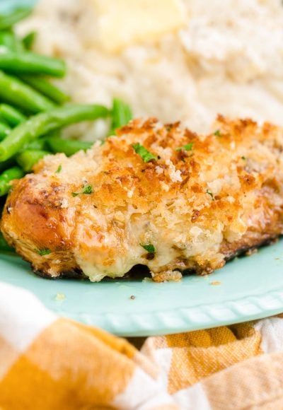 Close up photo of parmesan crusted chicken on a blue plate with mashed potatoes and green beans.