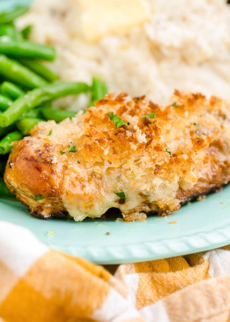 Close up photo of parmesan crusted chicken on a blue plate with mashed potatoes and green beans.