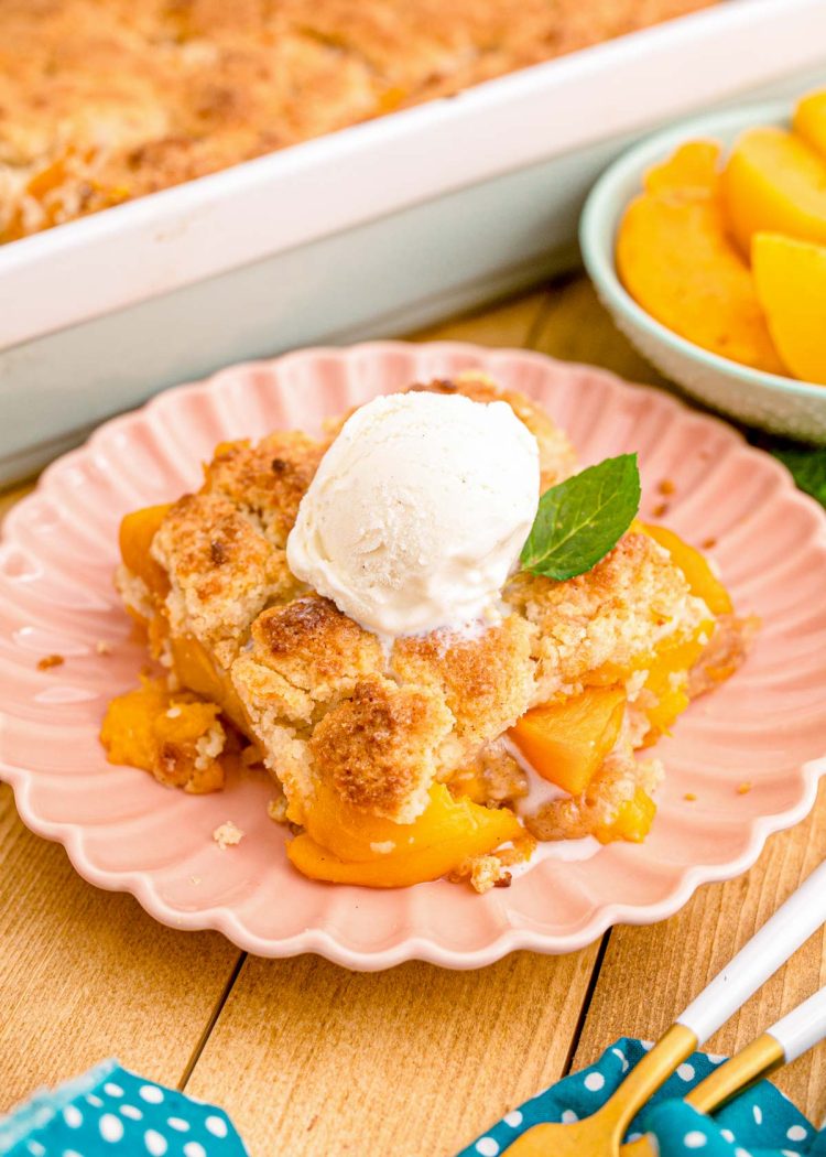 Close up photo of a slice of peach cobbler on a pink plate on a blue napkin.