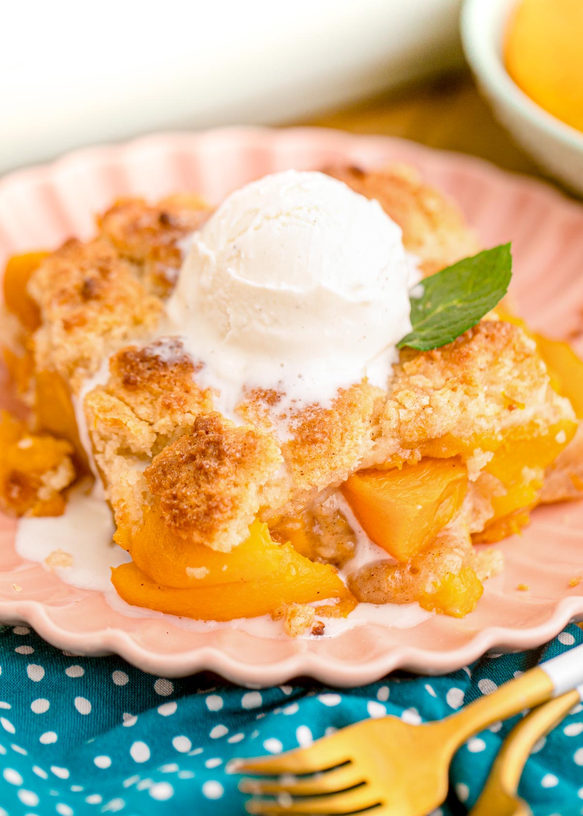 Close up photo of a slice of peach cobbler on a pink plate on a blue napkin.