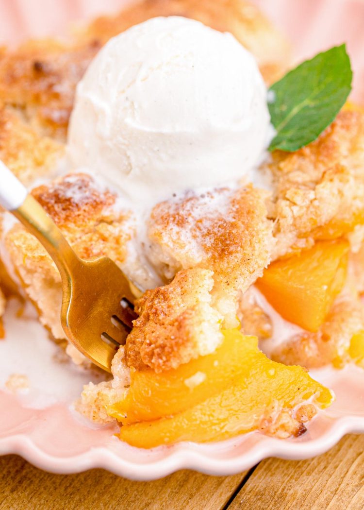 A fork taking a bite out of a slice of peach cobbler.