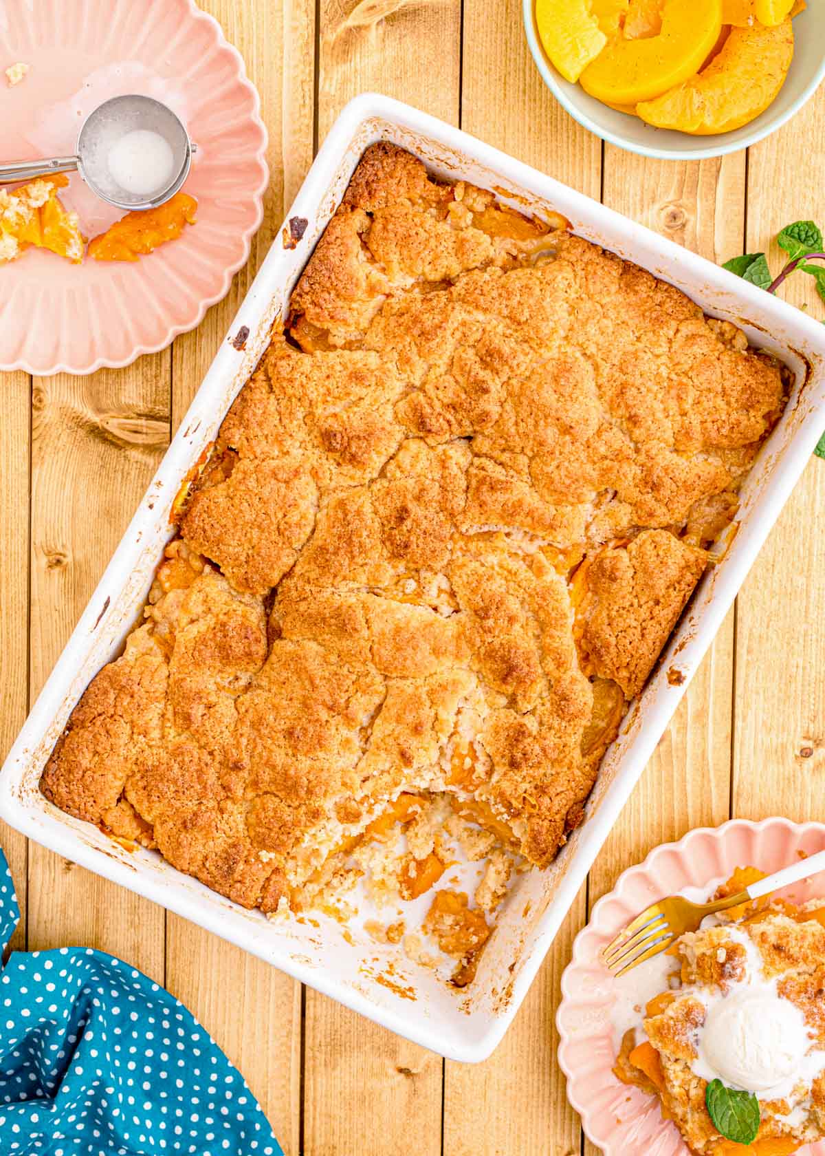 Peach cobbler in a white baking dish on a wooden table.