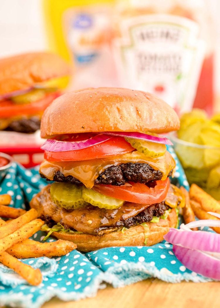 Close up of a smash burger on a blue napkin with condiment bottles in the background.