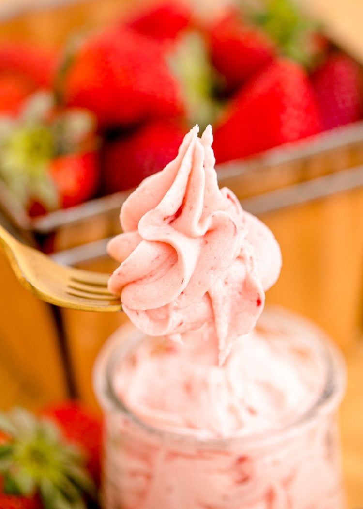 A fork lifting a bite of strawberry buttercream frosting out of a bowl.