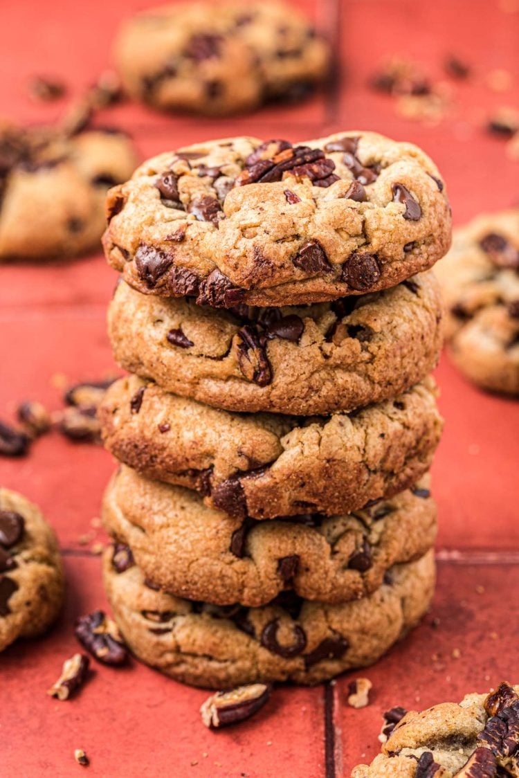 A stack of 5 brown butter pecan chocolate chip cookies on a red surface.