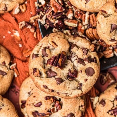 Brown Butter Pecan Chocolate Chip Cookies on a red surface with chopped pecans.