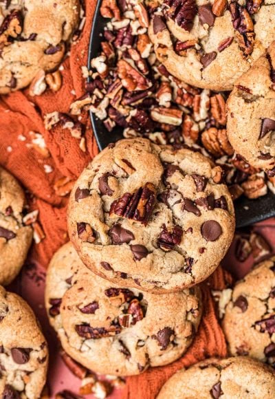 Brown Butter Pecan Chocolate Chip Cookies on a red surface with chopped pecans.
