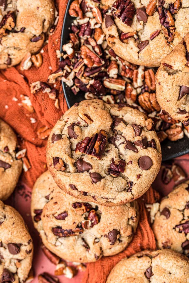 Brown Butter Pecan Chocolate Chip Cookies on a red surface with chopped pecans.