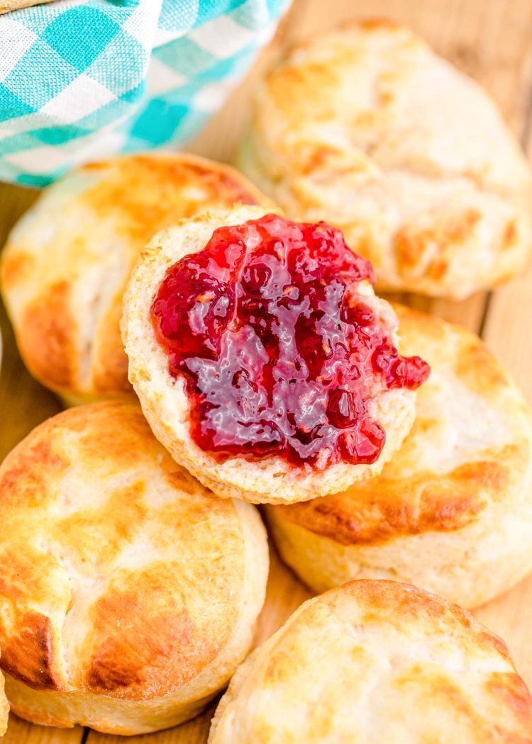 Jelly on a buttermilk biscuit piled on more biscuits on a wooden table.