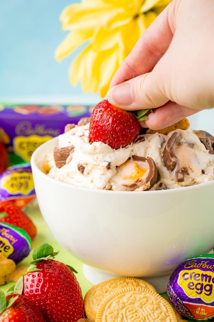 A woman's hand dipping a strawberry in cadbury creme egg dip.