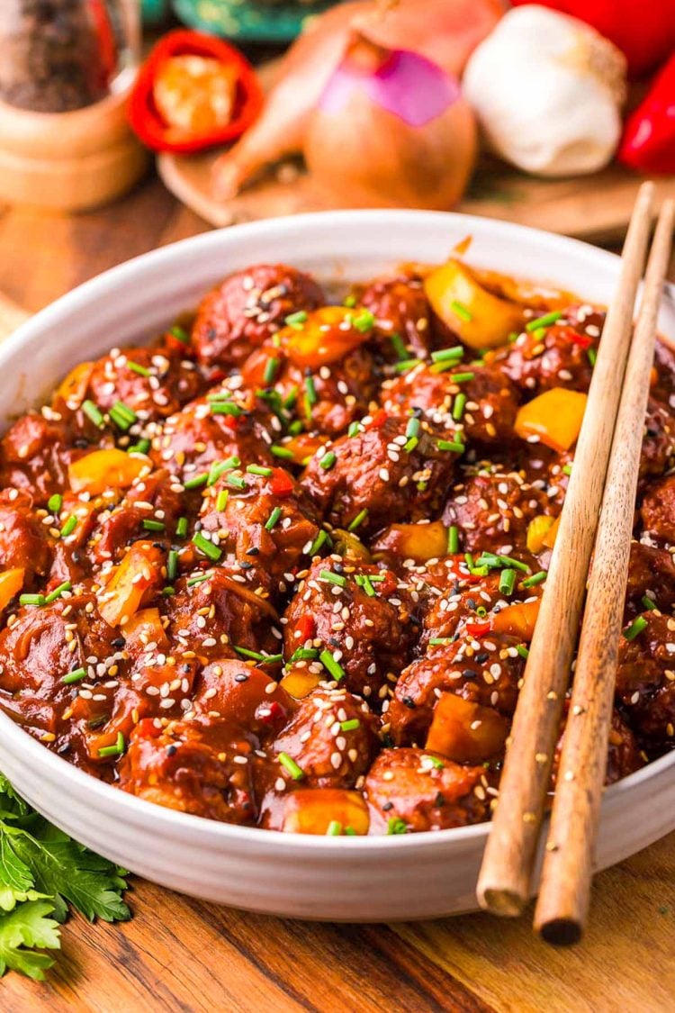 Close up of chicken manchurian in white bowl on a wooden table with chopsticks resting together on top of the bowl.