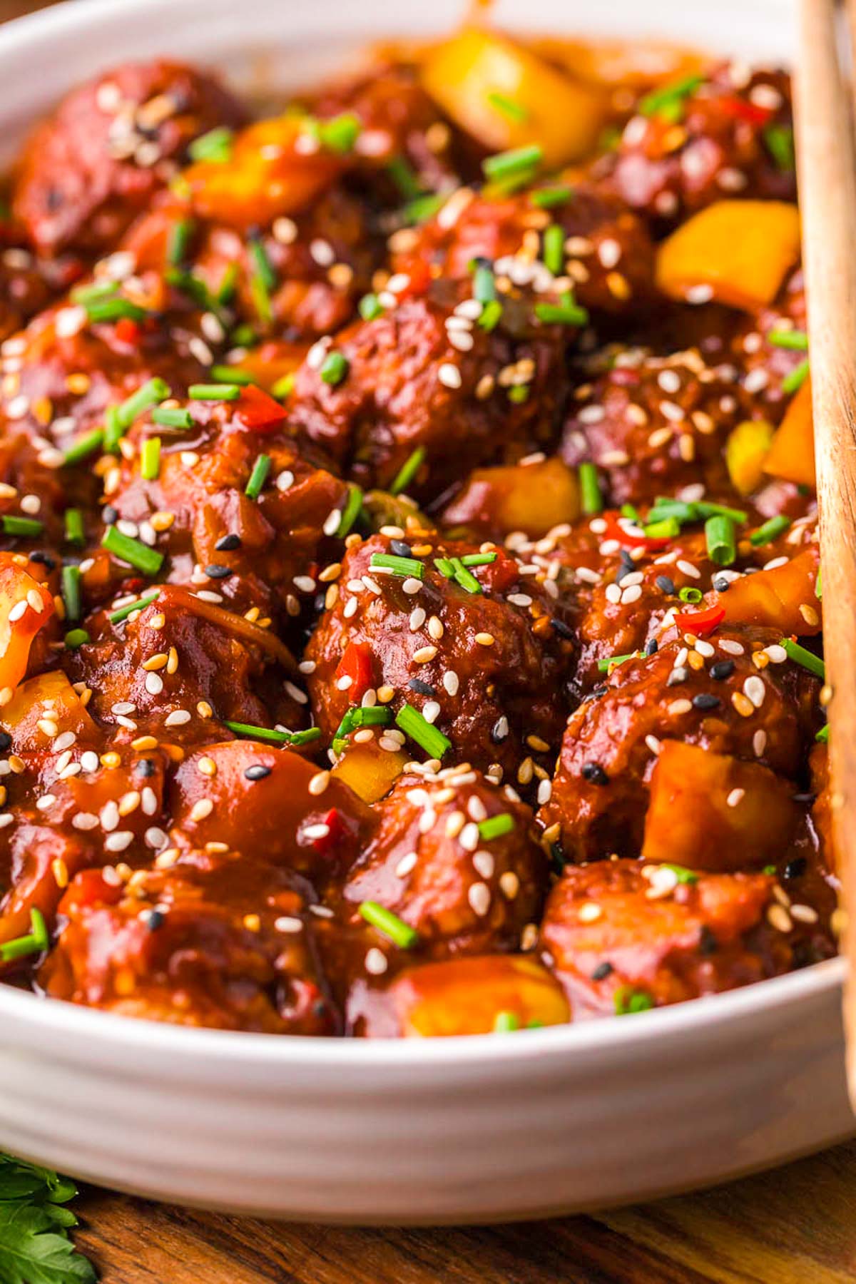 Close up of chicken manchurian in white bowl on a wooden table with chopsticks resting together on top of the bowl.
