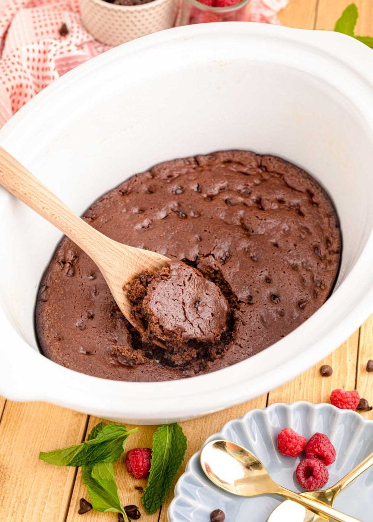 Chocolate cake being scooped out of a white crockpot.